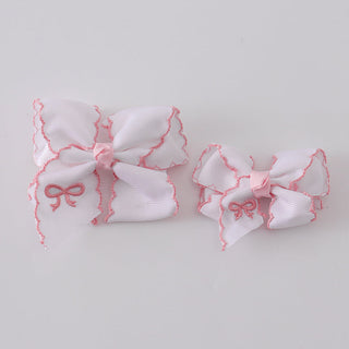 Two white hair bows with pink trim on a light gray background