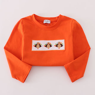 Orange long sleeve with an embroidery of three turkeys on a white background
