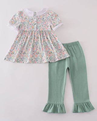 Children's floral top and green pants set on a light gray background