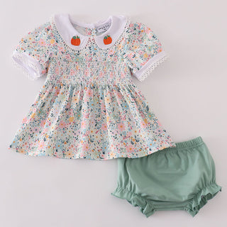 Floral top with orange accents and green bloomers on a light gray background