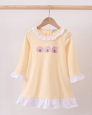 Yellow dress with white ruffled collar and hem on a wooden hanger against a beige background