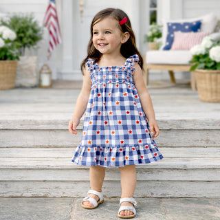 Child wearing a blue checkered dress with red and white stars on a wooden porch.