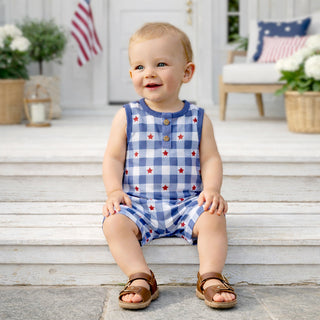 Child wearing a blue checkered romper with red stars sitting on steps outdoors.