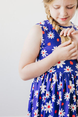 Young girl in a blue floral dress braiding her hair against a plain background