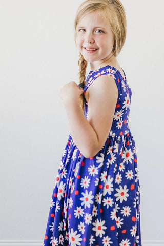 Young girl wearing a blue dress with white floral patterns on a plain background