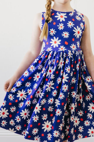 Child wearing a blue dress with white floral patterns on a plain background