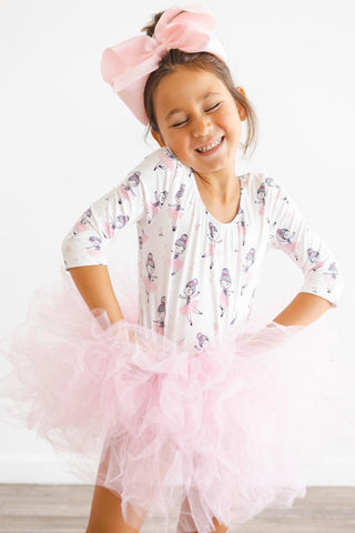 Young girl in a pink ballerina print tutu leotard with a large bow on her head, smiling.