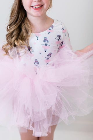 Young girl wearing a pink tutu leotard with ballerina  print on a plain background