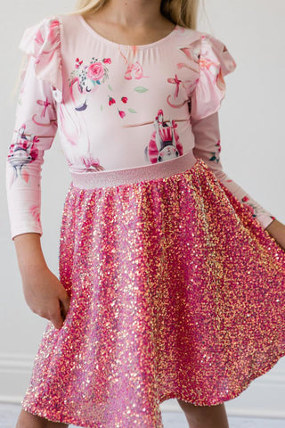 Child wearing a pink leotard with floral and ballerina designs and a sequined skirt.