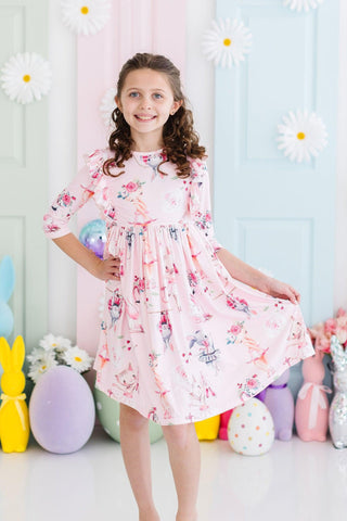 Young girl in a ballerina print dress standing in front of a colorful balloon and flower backdrop.