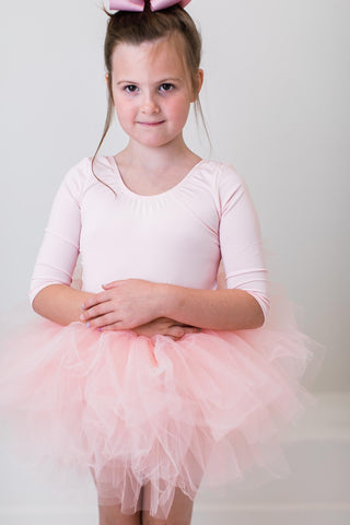 Young girl in a pink ballet outfit with a tutu on a plain background