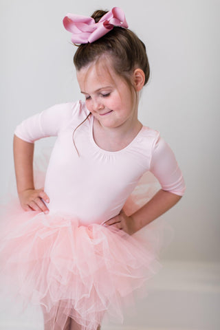 Young girl in a pink ballet outfit with a bow in her hair against a plain background