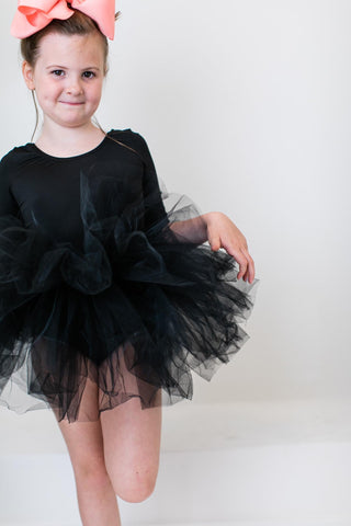 Young girl wearing a black leotard with a tutu skirt on a white background