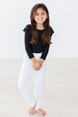 Young girl wearing a black long-sleeve leotard and white pants on a light background