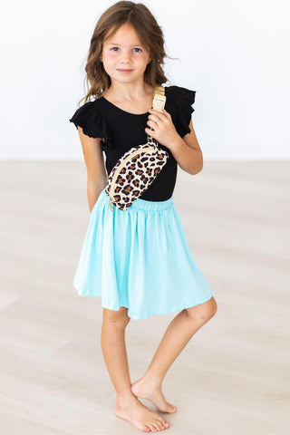 Young girl wearing a black leotard and light blue skirt with a leopard print bag on a plain background