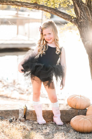 Young girl in a black tutu leotard standing outdoors with pumpkins and a tree in the background