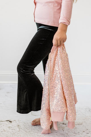 Person wearing black pants and holding pink sequin jacket on a light background