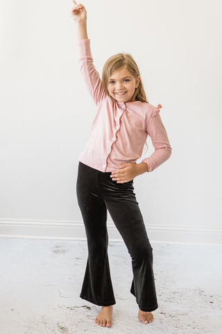 Young girl wearing a pink blouse and black pants against a white background