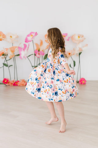Child in a floral dress standing in front of decorative flowers on a light background
