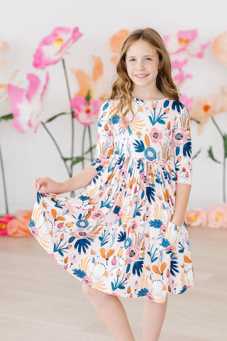 Young girl wearing a floral dress with a colorful pattern against a floral backdrop.