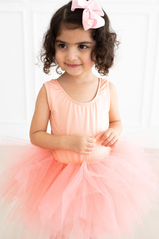 Young girl in a pink leotard with a bow on her head against a white background