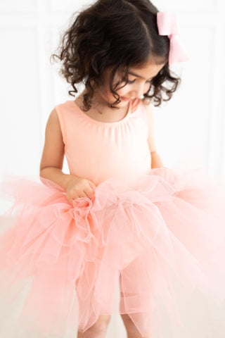 Young girl in a pink leotard with a large bow on a white background