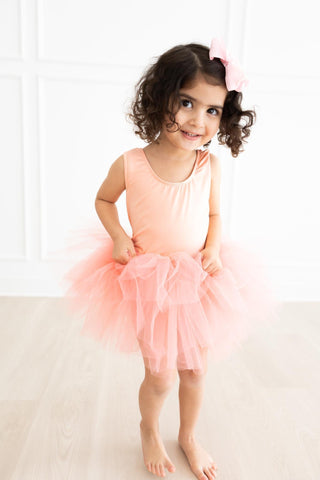 Young girl in a pink tutu leotard standing against a white background