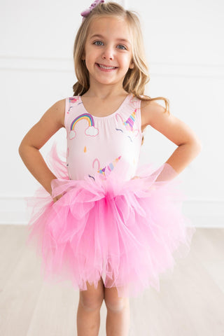 Young girl wearing a pink leotard with rainbow and cloud designs on a white background