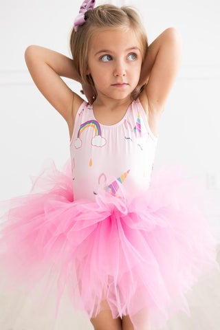 Young girl wearing a pink leotard with colorful designs and a pink tutu skirt on a light background
