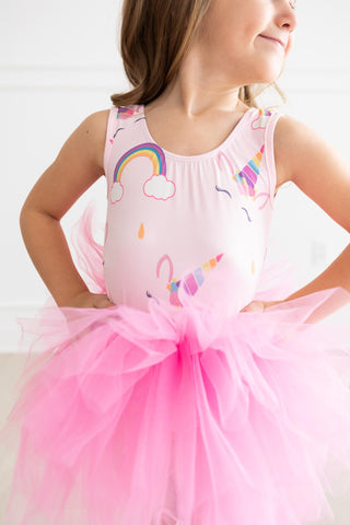 Young girl wearing a pink leotard with rainbow and cloud designs on a white background