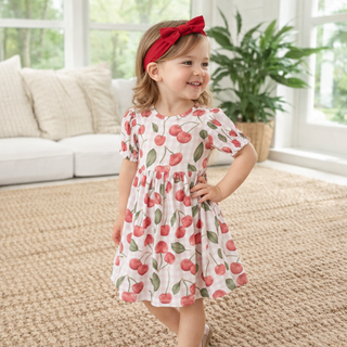 Young girl in a cherry-patterned dress standing in a living room.
