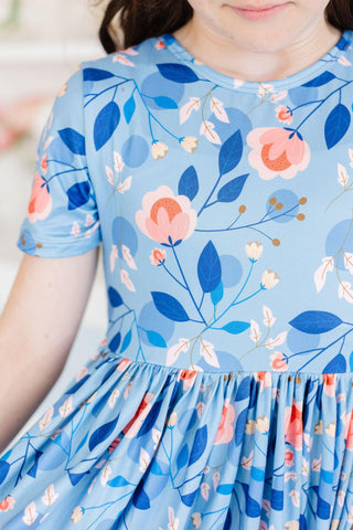 Child wearing a blue floral dress with pink flowers and green leaves.