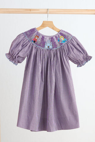 A purple hand smocked gingham dress for toddlers, hanging on a wooden hanger, featuring short sleeves and a collar.