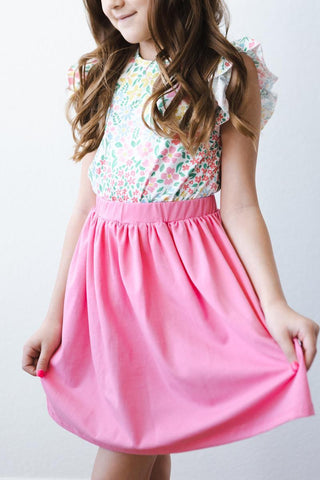Young girl wearing a floral top and pink skirt against a white background