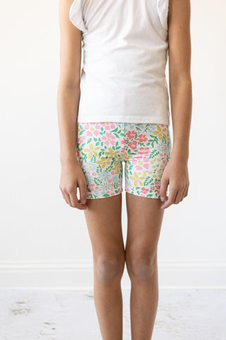 Person wearing floral shorts and a white shirt on a light wooden floor.