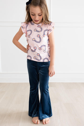 Young girl wearing a patterned top and blue pants on a white background