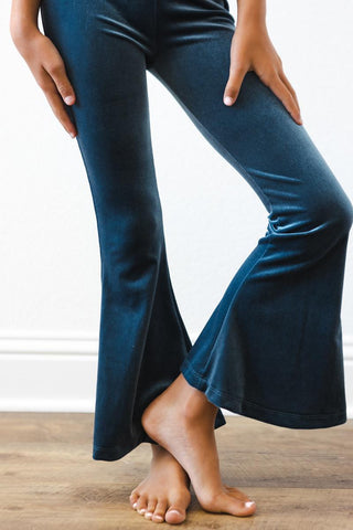 Person wearing blue flared pants standing on a wooden floor with a white wall background