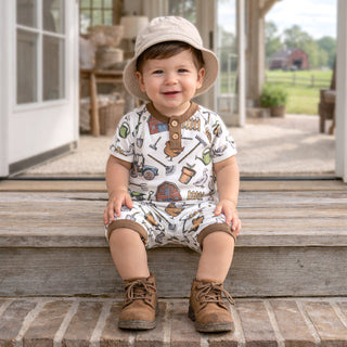 Child wearing a farm themed patterned romper and hat sitting on steps outdoors.