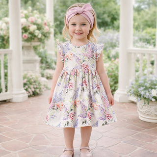Young girl in a floral dress standing on a stone patio with flowers and columns in the background