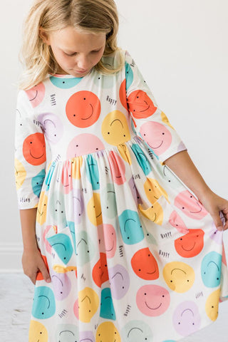 Child wearing a colorful dress with smiley face patterns on a white background