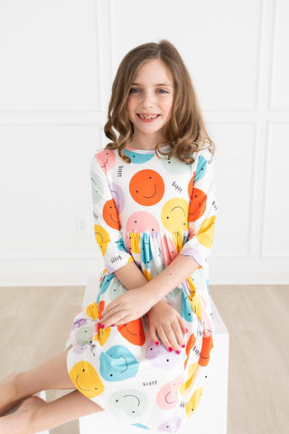 Young girl wearing a colorful dress with smiley face designs on a white background