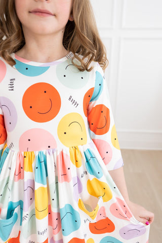 Child wearing a colorful dress with smiley face patterns on a white background