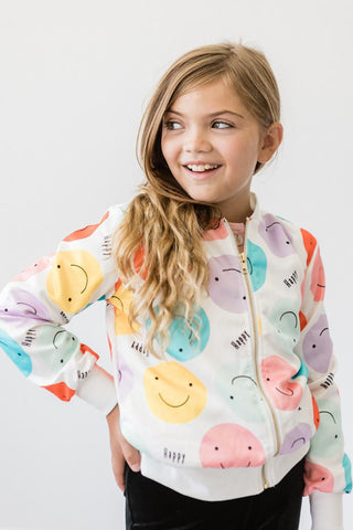 Young girl wearing a colorful jacket with smiley face patterns on a plain background
