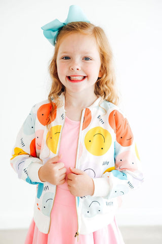 Young girl wearing a colorful cartoon-themed jacket with a white background