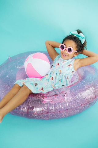 Child on a pink inflatable ring with a beach ball against a blue background
