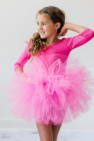 Young girl wearing a bright pink leotard with a tutu skirt against a white background