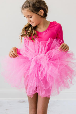 Young girl wearing a bright pink leotard with a tutu skirt on a light gray background