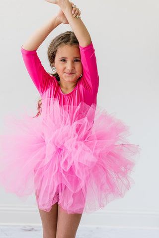 Young girl in a pink leotard with a tutu standing against a white background