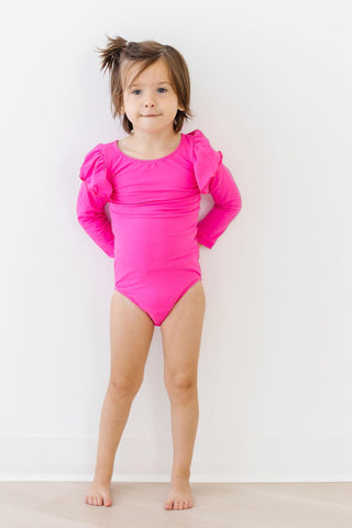 Young girl wearing a bright pink leotard with ruffled sleeves against a white background