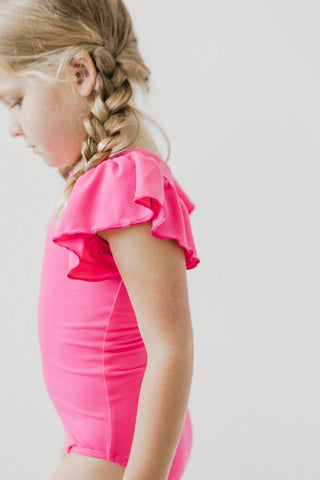 Child wearing a bright pink leotard with ruffled sleeves on a plain background